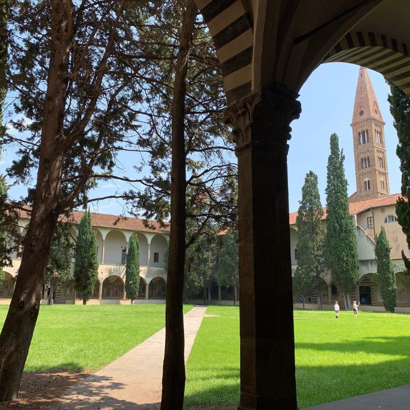 A photo of one of Santa Maria Novella's interior grassy cloisters, with its tower visible above the rooftop.